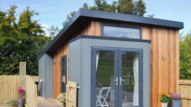 Une structure moderne en bois, dotée d’une grande porte-fenêtre coulissante, d’une petite terrasse et de plantes en pot.