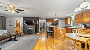 A modern kitchen with wooden cabinets, a dining area with a round table, and a living room with a sofa and fireplace. - Steps to the Beaches of Lake Erie 4BR, 3BA Home (Dunkirk)
