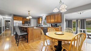 A modern kitchen with wooden cabinets, a stainless steel refrigerator, and a dining area with a wooden table and chairs. - Steps to the Beaches of Lake Erie 4BR, 3BA Home (Dunkirk)