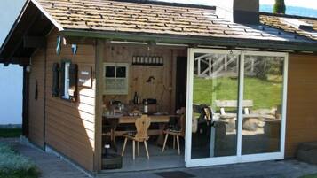 Une cabane en bois comprenant un coin repas, des portes-fenêtres coulissantes et une cheminée.