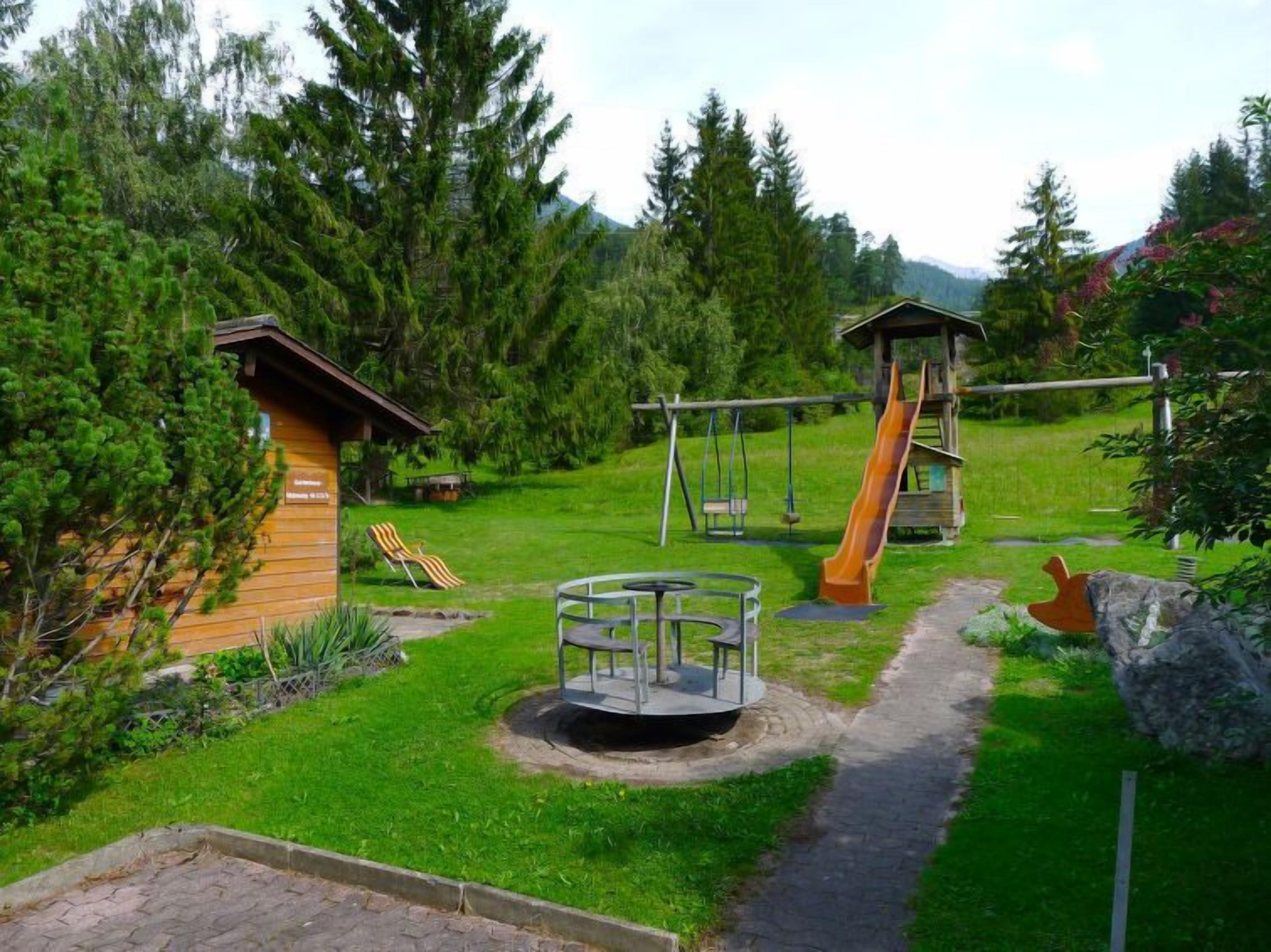 Une aire de jeux avec des balançoires, un toboggan et un espace de jeux circulaire où l’on peut s’asseoir.
