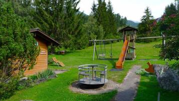 Une aire de jeux avec des balançoires, un toboggan et un espace de jeux circulaire où l’on peut s’asseoir.