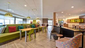 A modern hotel lobby with green seating, wooden tables, and a reception desk. - Home2 Suites by Hilton Eau Claire South (Eau Claire)