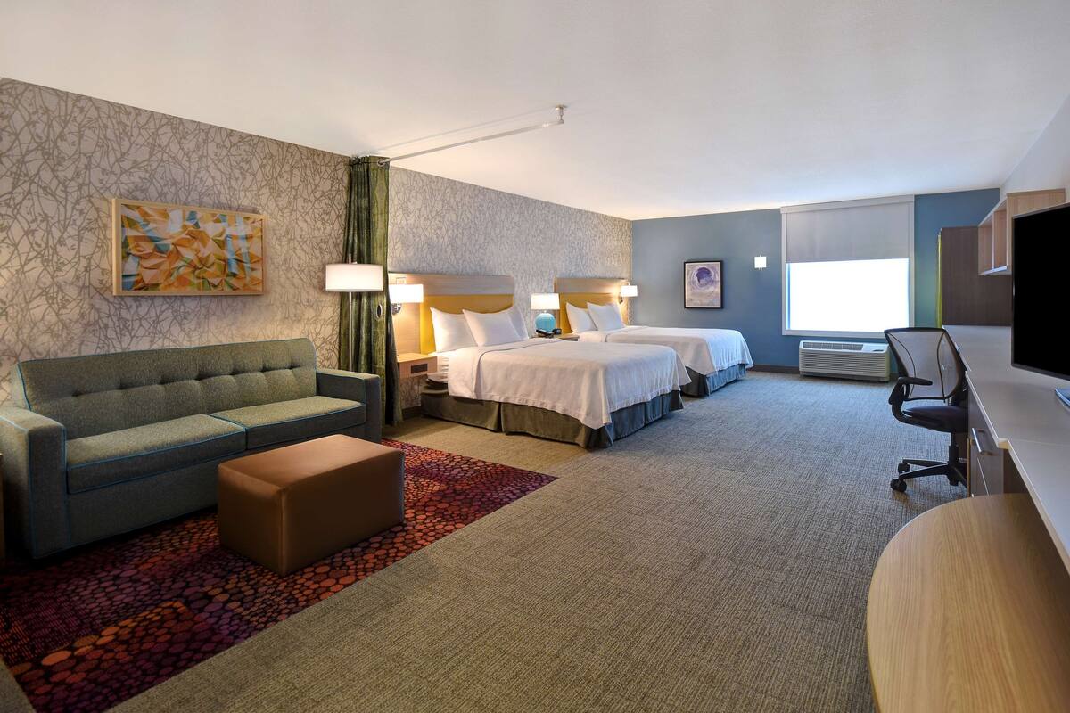 Habitación de hotel con sofá, dos camas, escritorio y televisor.