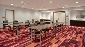 A conference room with multiple tables and chairs, a patterned carpet, and a large painting on the wall.