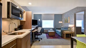 A modern kitchen with a microwave, sink, and a flat-screen TV. There is a seating area with a sofa and a small table. - Home2 Suites by Hilton Eau Claire South (Eau Claire)
