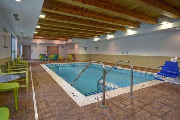 Una piscina interior con carriles delimitados, una escalera de acceso y una zona de estar con sillas.