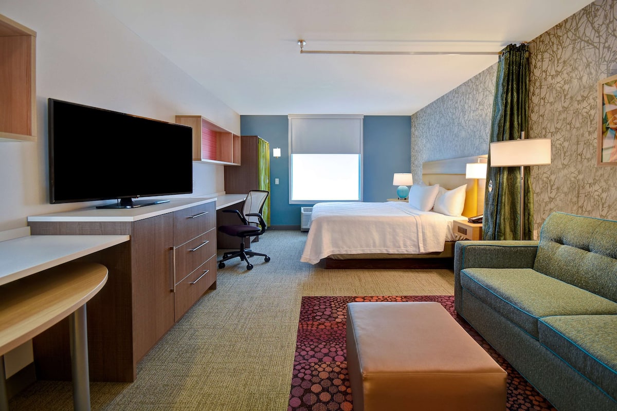 Una habitación de hotel con cama, escritorio, televisión, sofá y una silla.