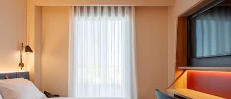 Quarto de hotel moderno com cama, escrivaninha e televisão.