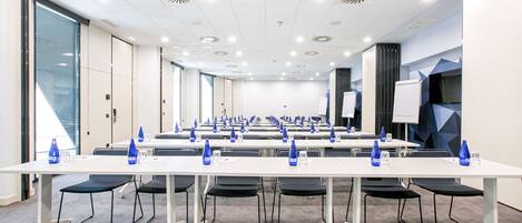 A conference room with white tables, black chairs, and blue water bottles.