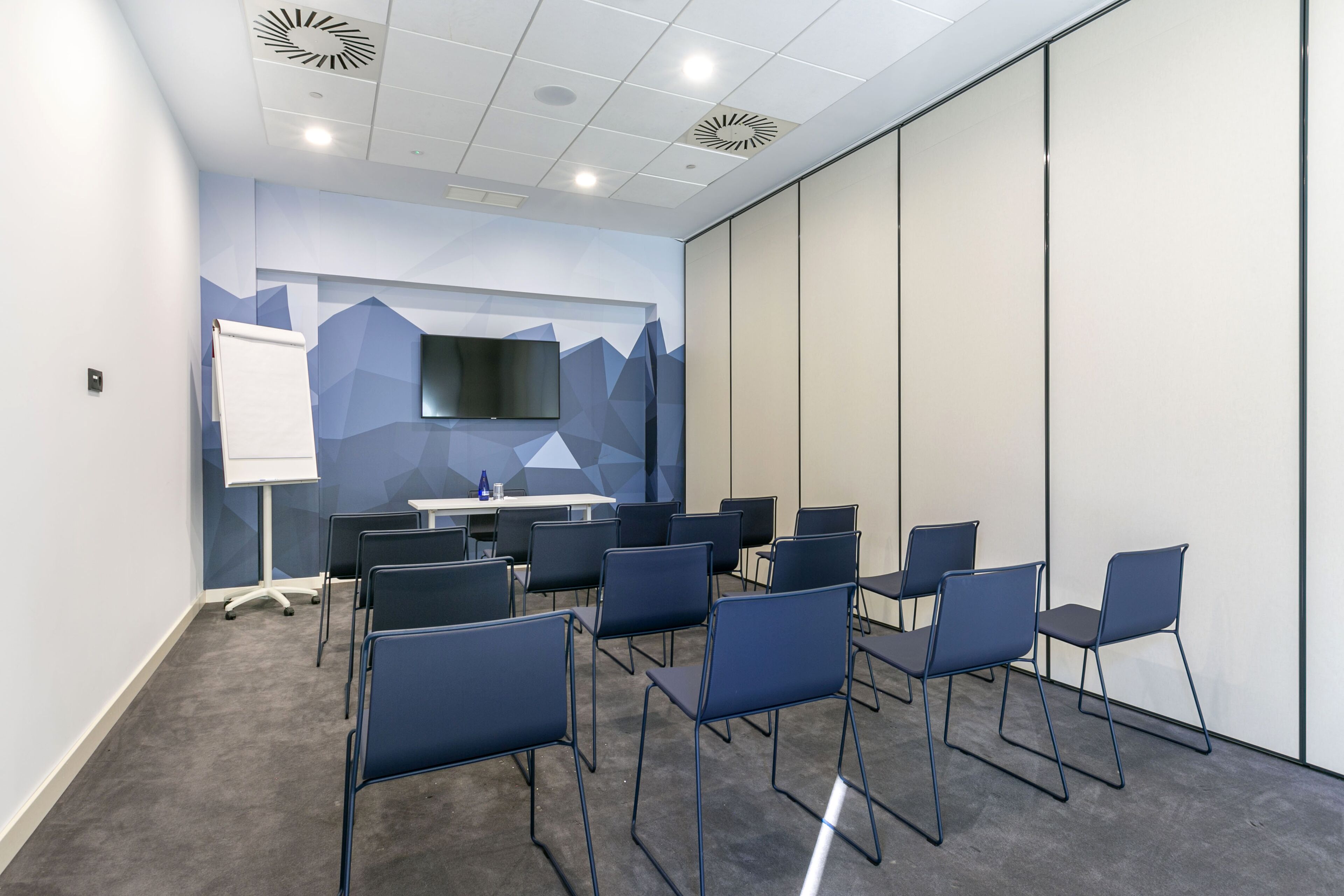 Un salón de conferencias con una pizarra, un televisor de pantalla plana y varias sillas dispuestas alrededor de una mesa.