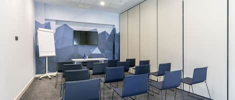 Una sala conferenze con una lavagna, un televisore a schermo piatto e numerosi posti a sedere disposti attorno a un tavolo.