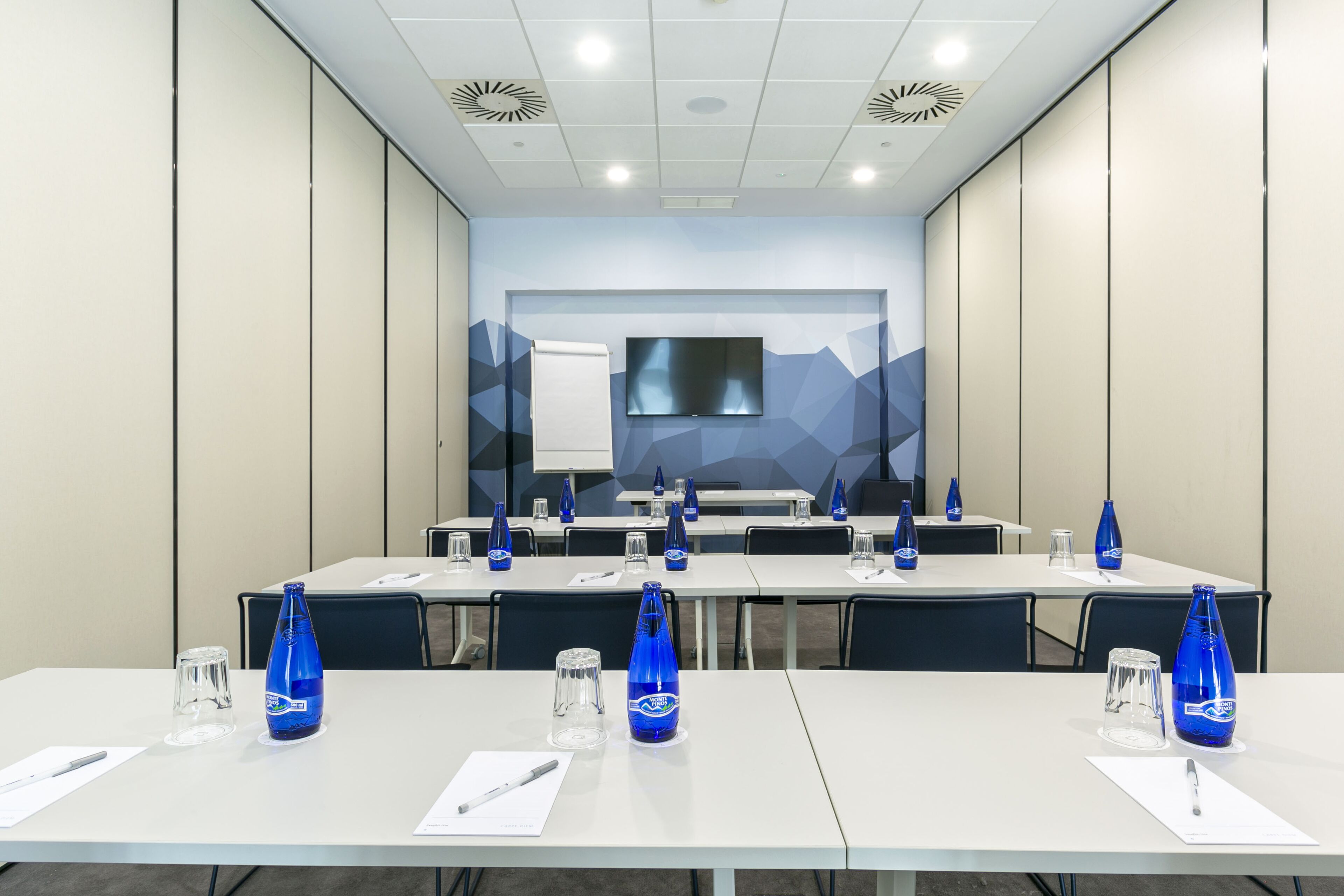 Un salón de conferencias con mesas, sillas y botellas de agua azules.