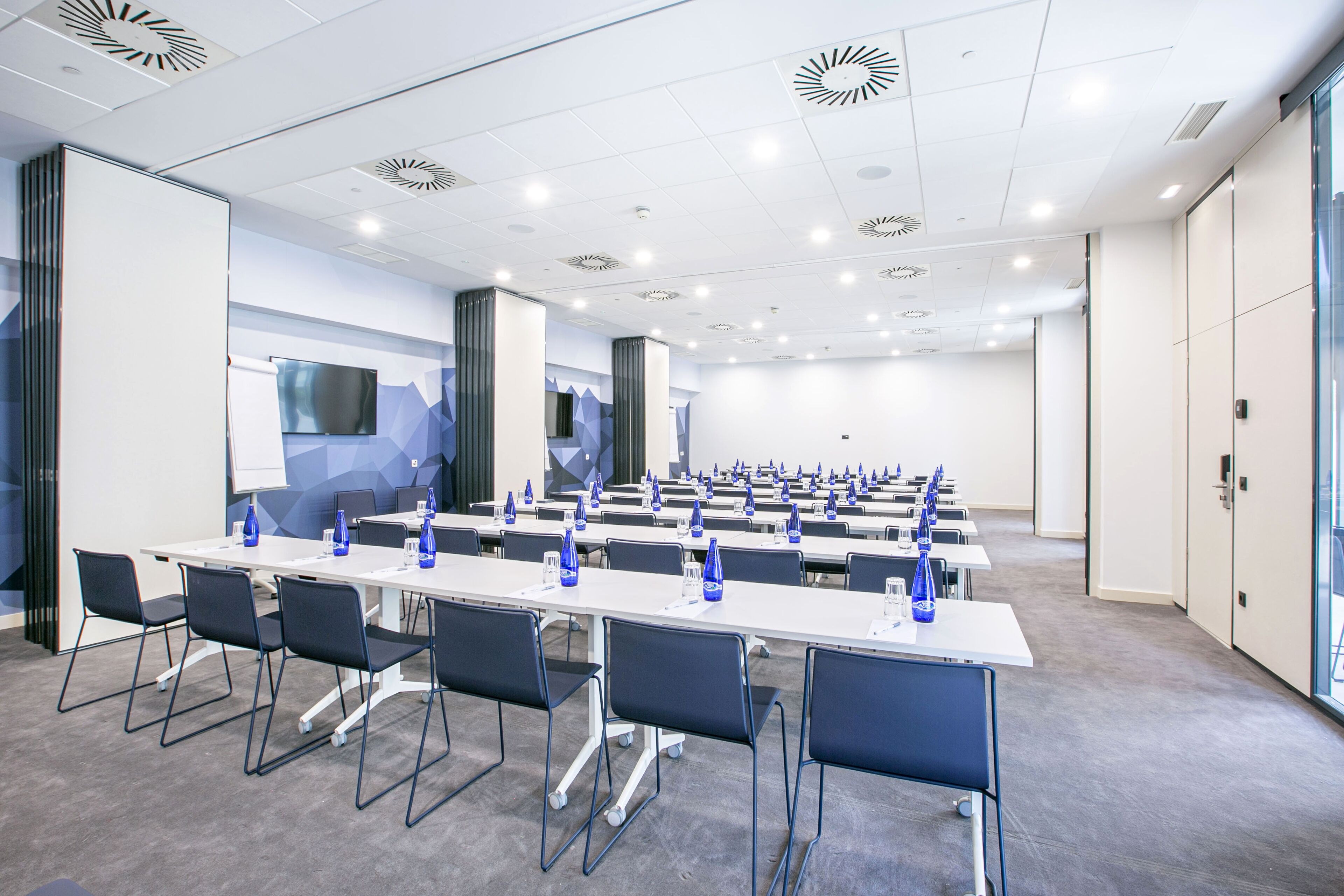 Un salón de conferencias con varias mesas, sillas y una pantalla grande.