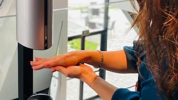 Una persona usando un dispositivo moderno y elegante, montado en la pared, probablemente un quiosco digital o pantalla interactiva, en un espacio interior bien iluminado con grandes ventanales.