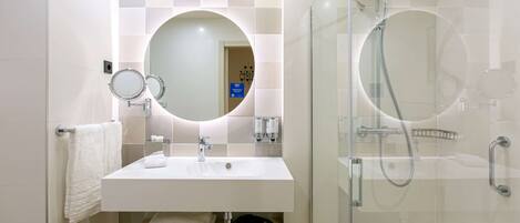Une salle de bain moderne avec un lavabo blanc, un miroir rond et une douche à parois de verre.