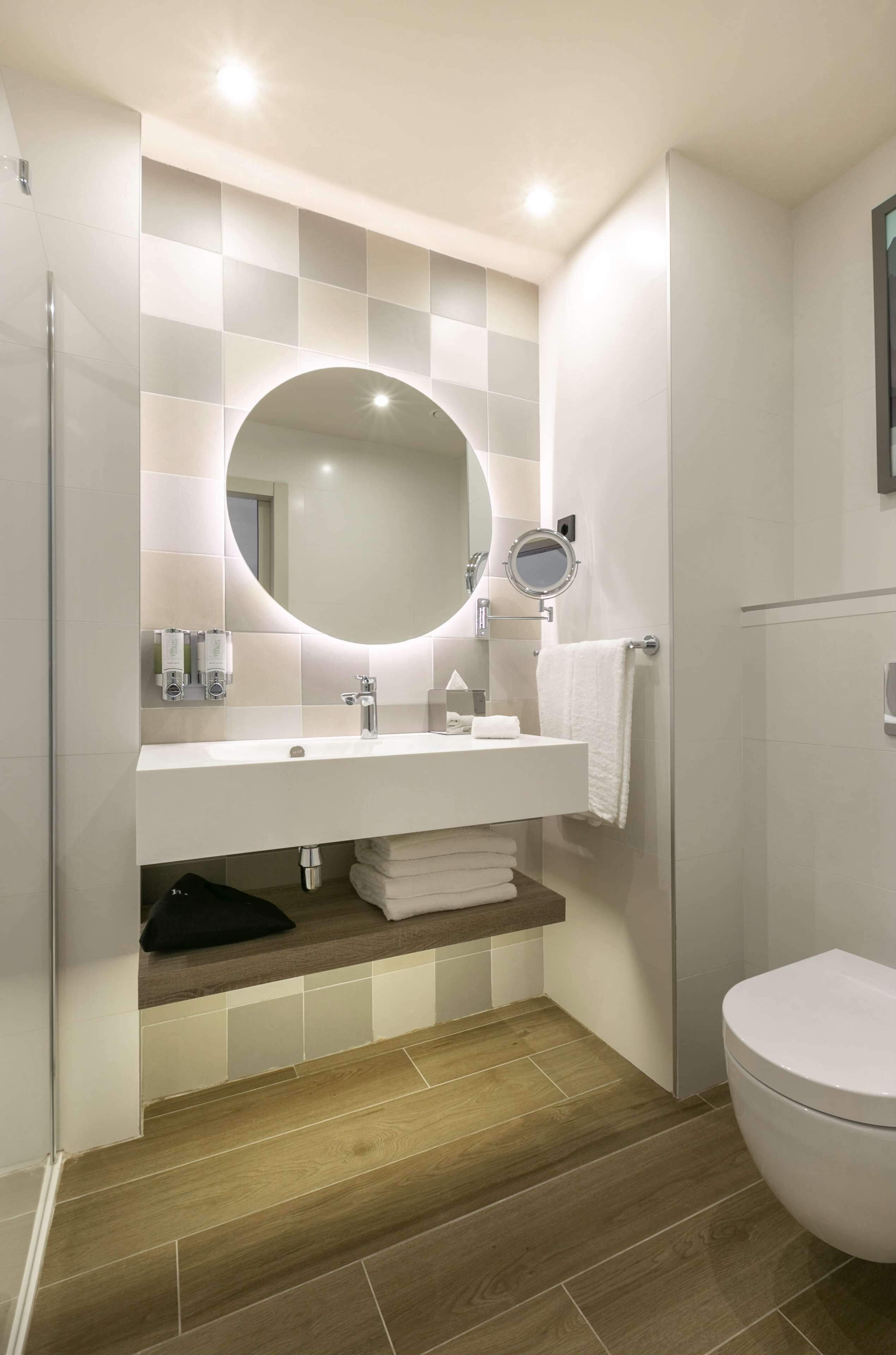 Un baño moderno con lavamanos, espejo y retrete blancos.