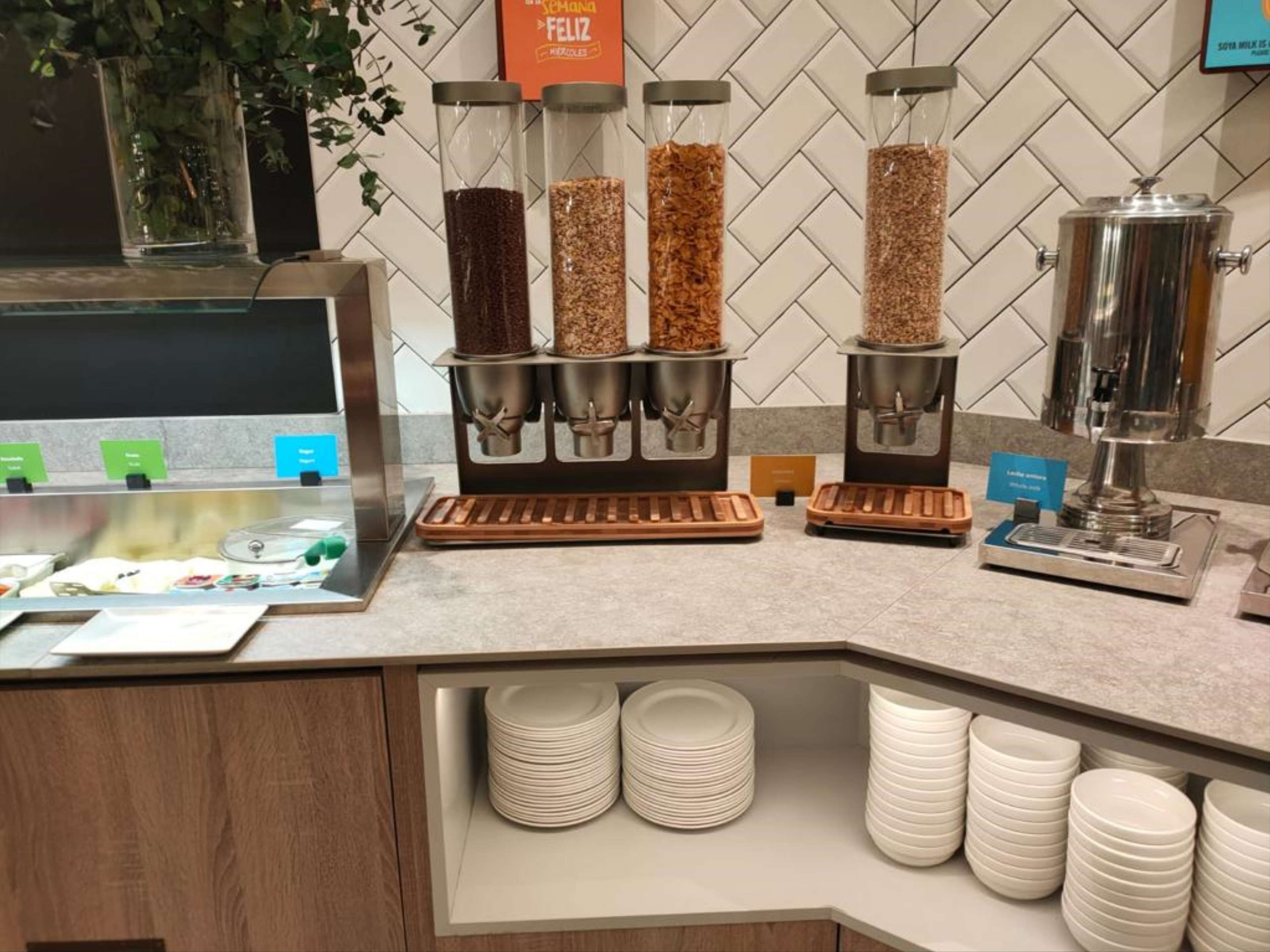 Un buffet pour le petit-déjeuner comprenant plusieurs distributeurs de café, un présentoir de fruits et des piles d’assiettes blanches.