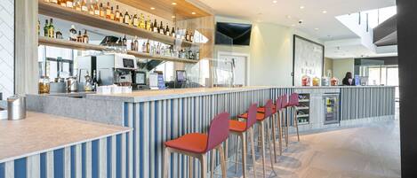 Zona de bar moderna con una barra larga, varios taburetes y una variedad de botellas en estanterías.