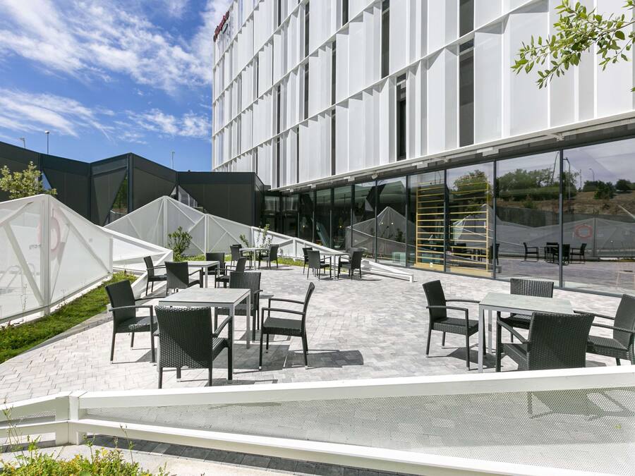 Un'area salotto esterna con tavoli e sedie, un edificio moderno con ampie finestre e un cielo sereno.