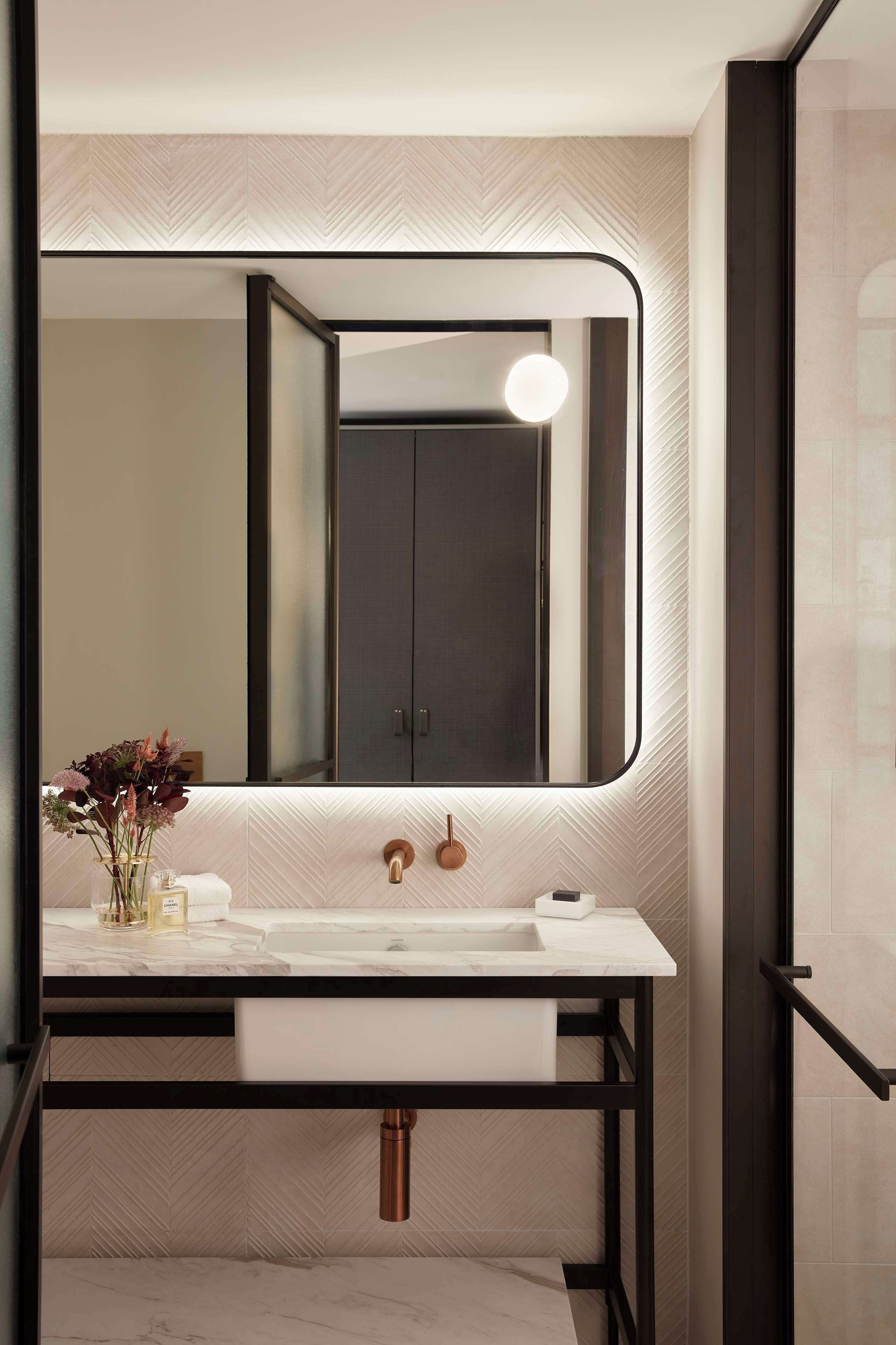 A modern bathroom with a large mirror, a white sink, and a towel rack.