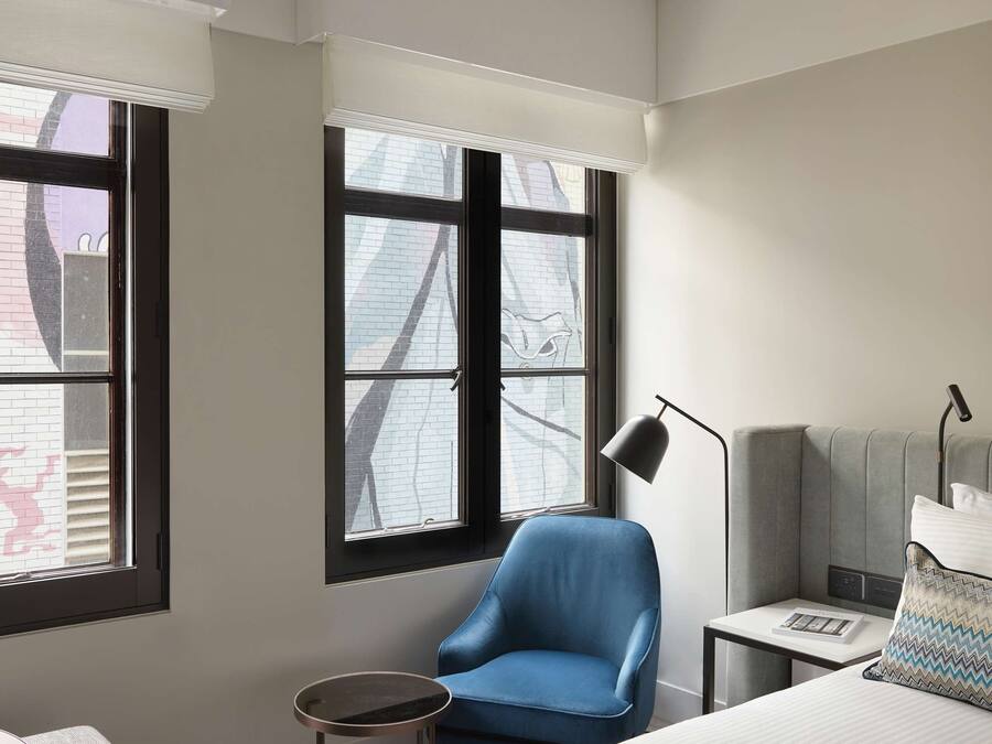 A hotel room with a bed, a desk, a chair, and two windows.