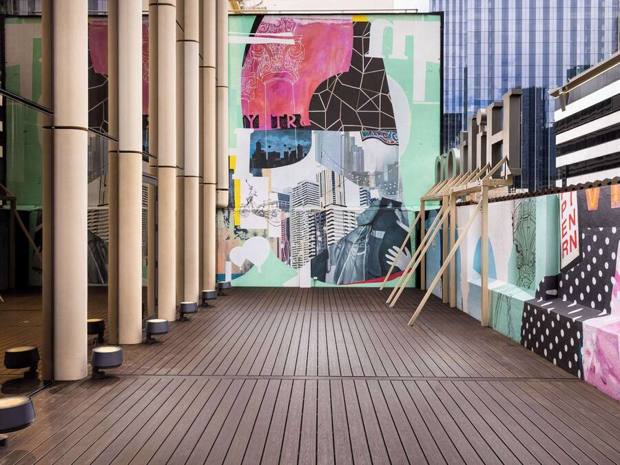 Un couloir doté d’un plancher en bois, de grandes colonnes et d’une fresque colorée aux motifs abstraits.