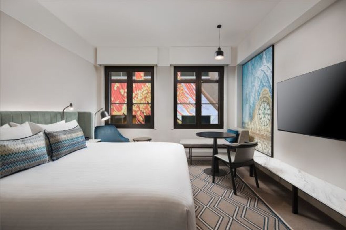 A modern hotel room with a large bed, a desk, and a TV.
