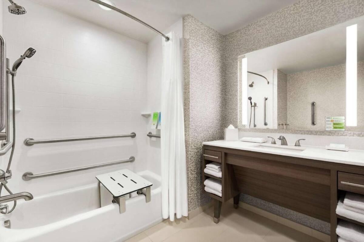 A modern bathroom with a walk-in shower, grab bars, a vanity with a mirror, and a bathtub.