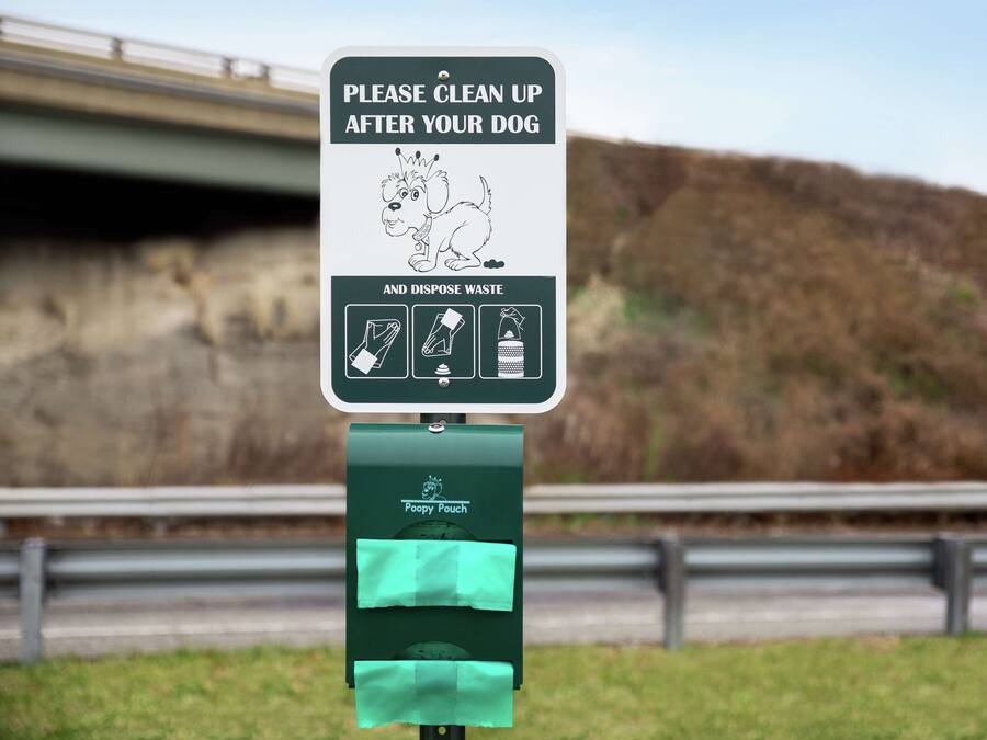 Een bordje met de instructie om na honden te ruimen en afval weg te gooien, met een Poopy Pouch bevestigd.