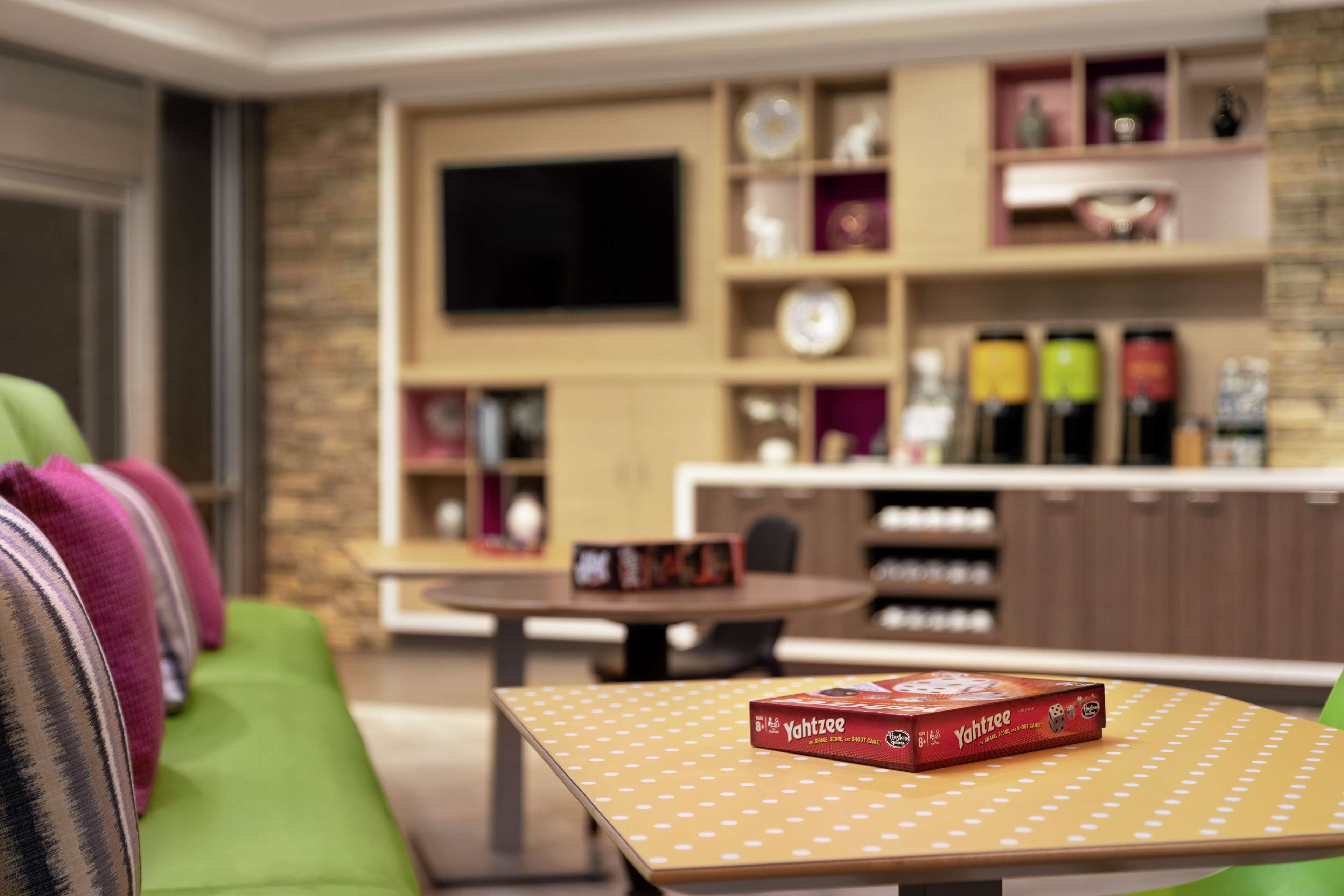 A cozy living room with a green sofa, a coffee table with a board game, and a bookshelf with various items.
