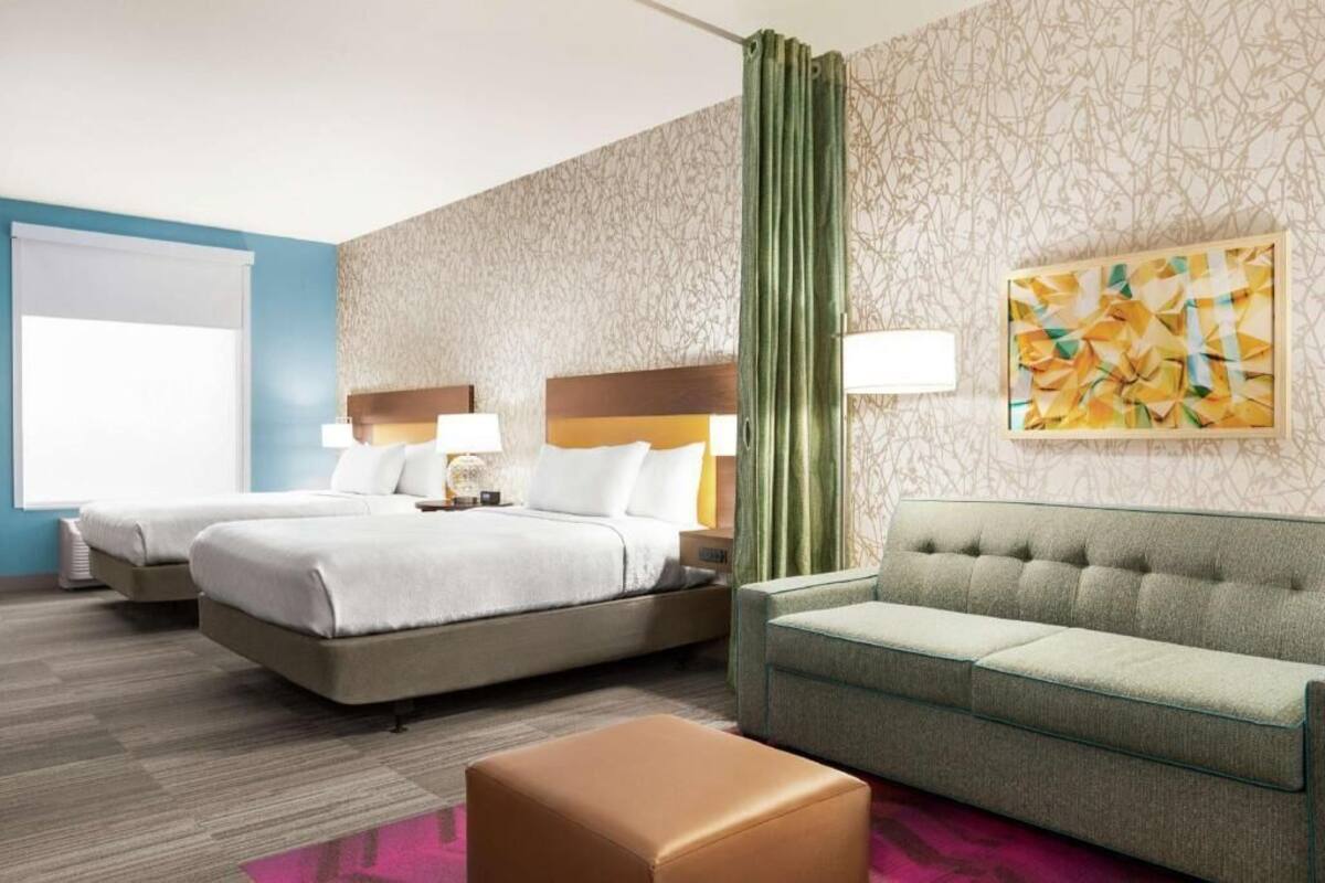 A hotel room with two beds, a sofa, a decorative wall, and a window.