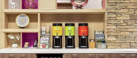 A coffee station with three coffee dispensers labeled 'GOURMET,' 'DECAF,' and 'HOT H2O.' There are also shelves with decorative items and a stone wall.