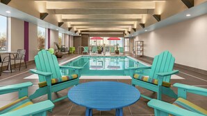 Zwembadgedeelte met turquoise Adirondack-stoelen en een blauwe tafel, omgeven door planten in potten en uitzicht op het zwembad.