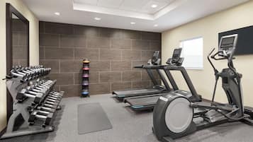 Une salle de sport équipée de tapis de course, de vélos elliptiques et de rangées de haltères.