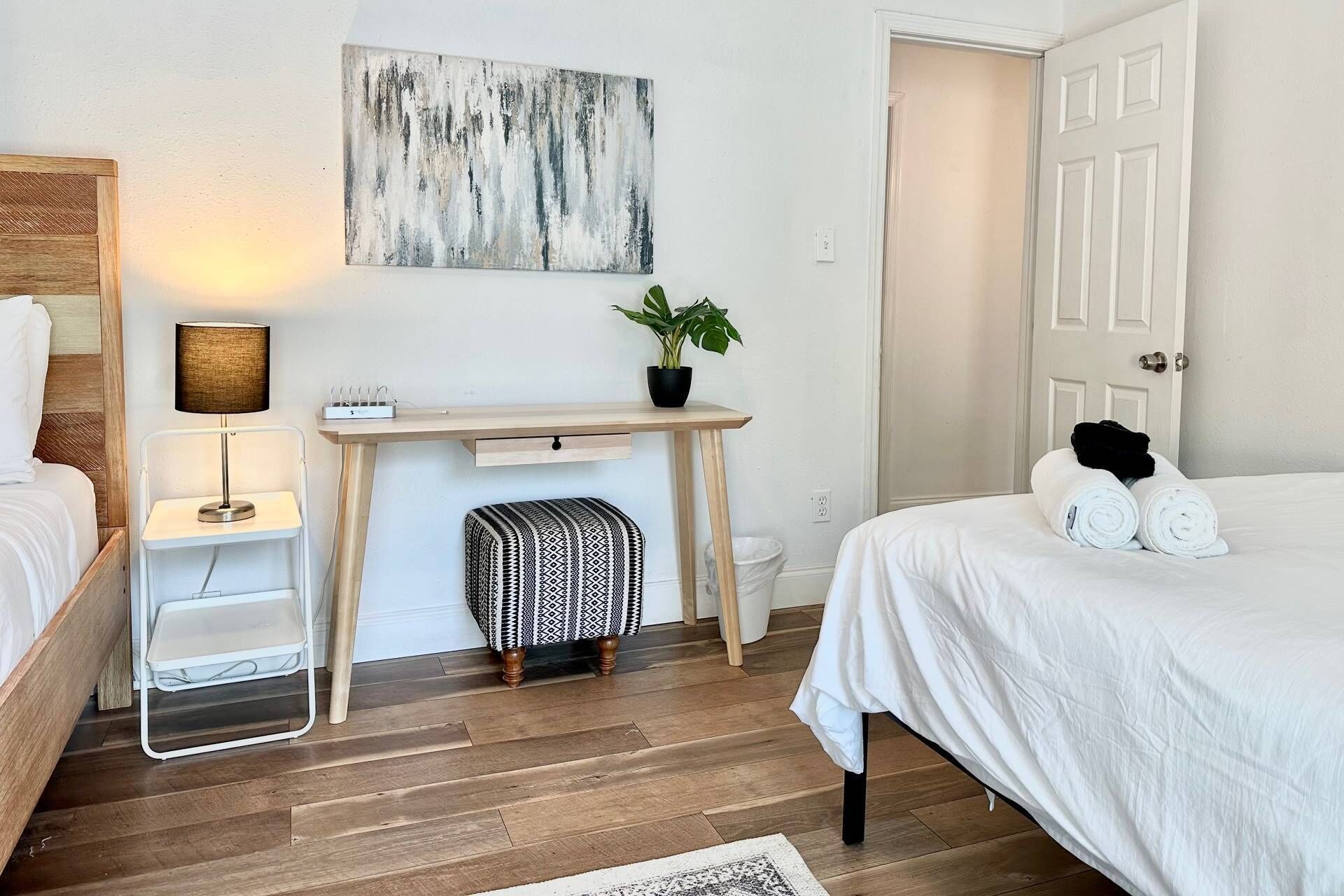 Ein Schlafzimmer mit einem Bett, einem Schreibtisch mit Pflanze, einer Lampe und einem Wandbild.