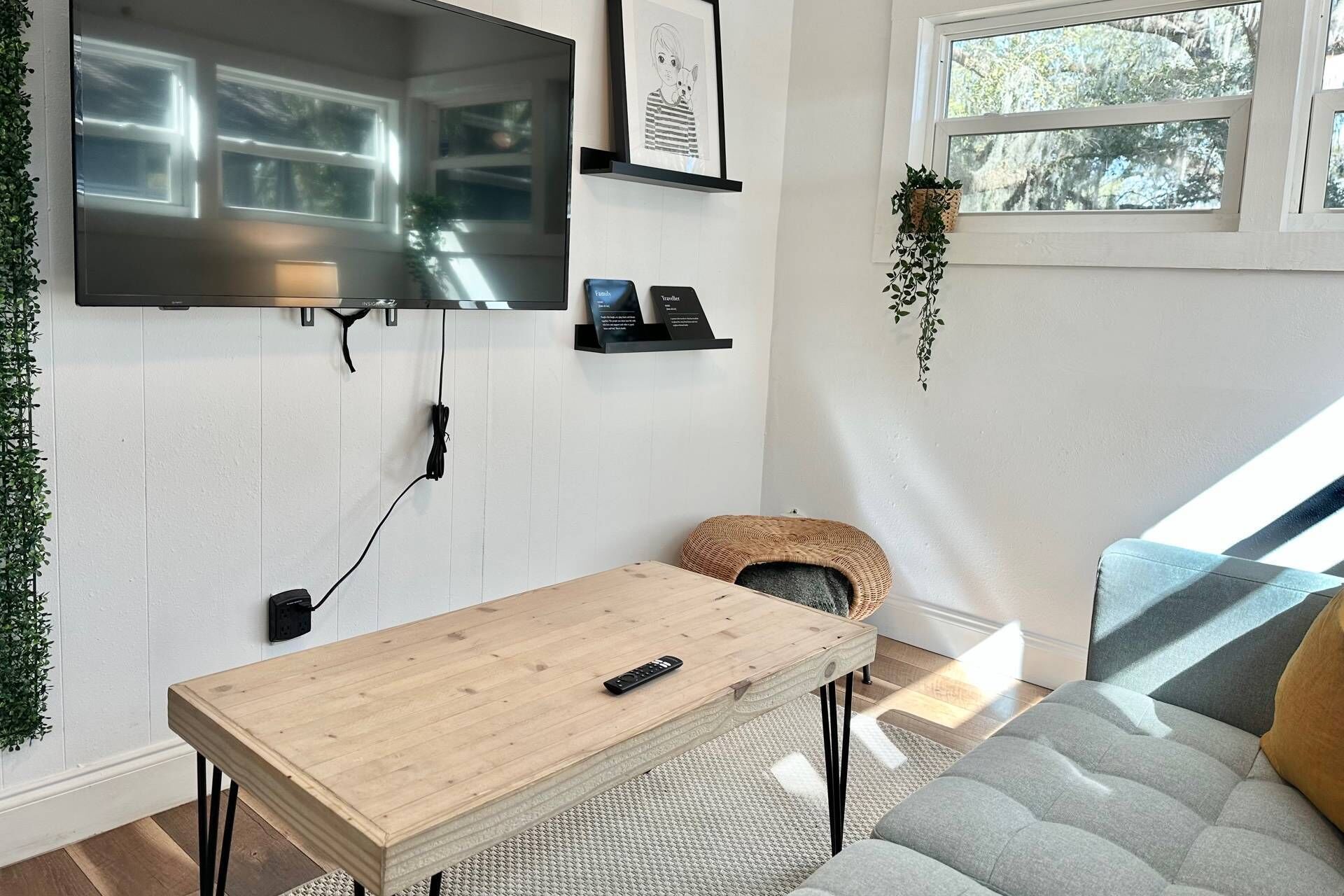 A modern living room with a wooden coffee table, a mounted TV, a wicker pouf, and a grey sofa.