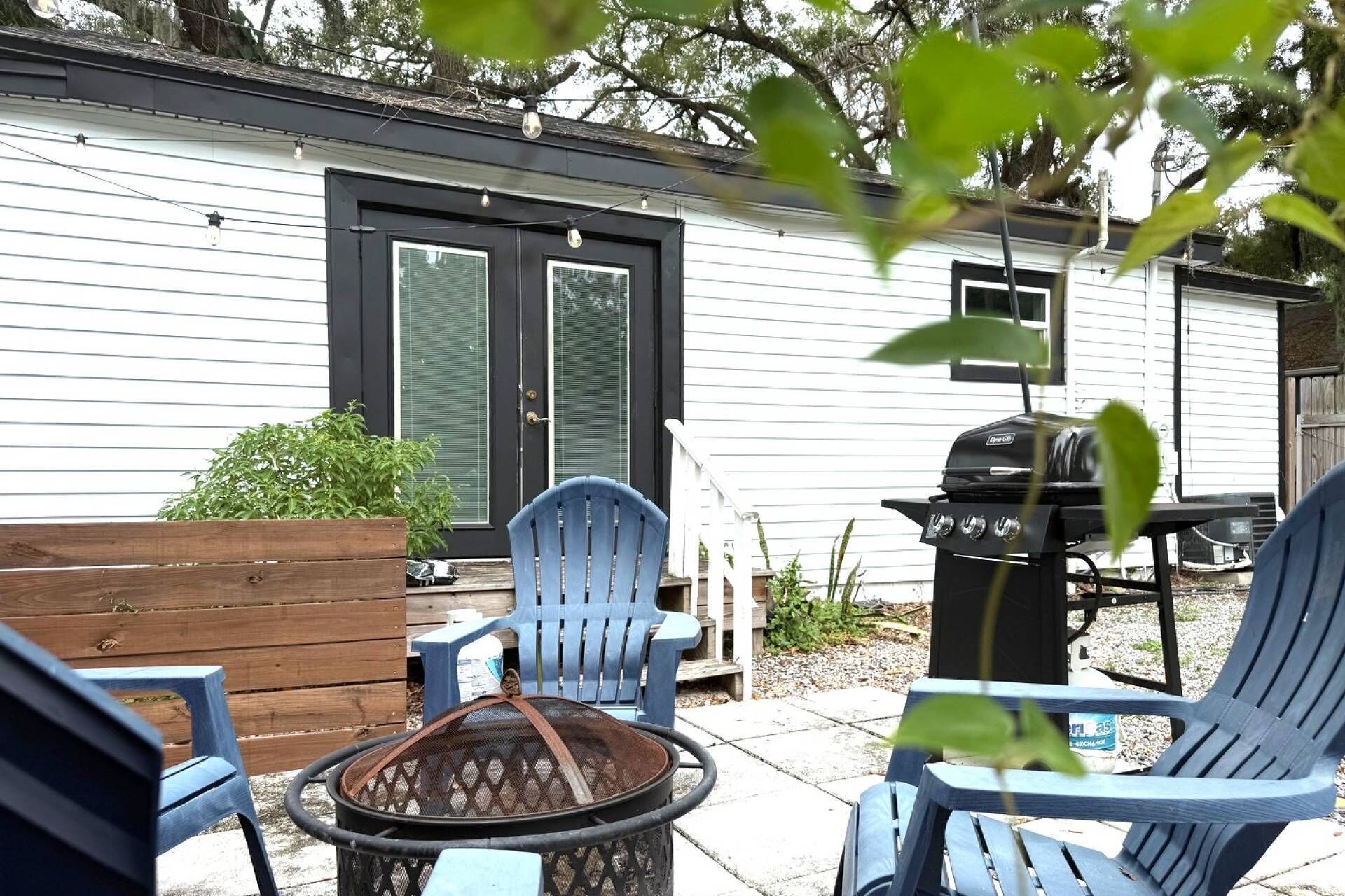 Une terrasse avec des chaises bleues, un barbecue et un jardinière en bois.