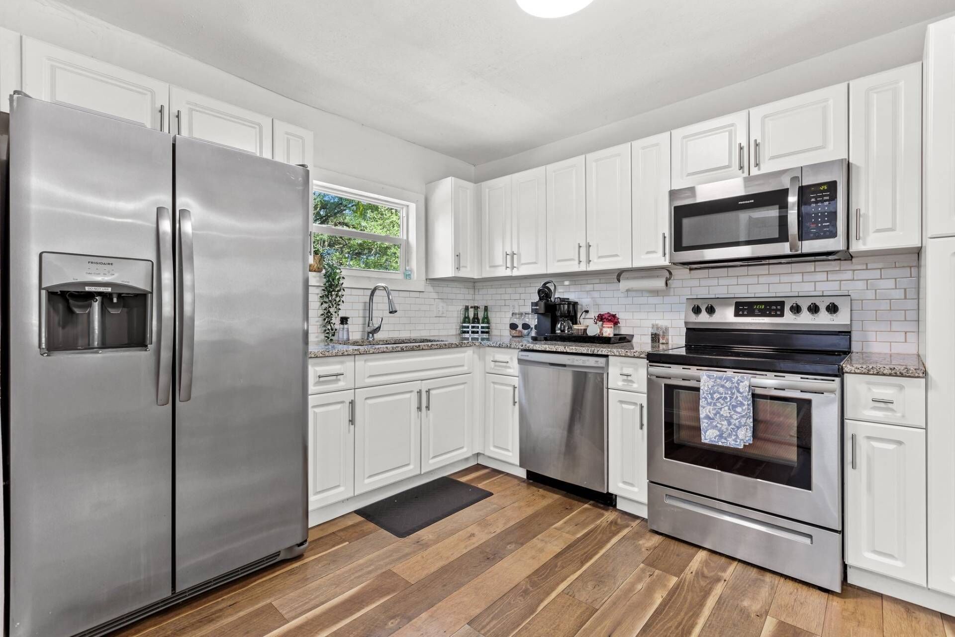 A modern kitchen with white cabinets, stainless steel appliances, and a wooden floor.