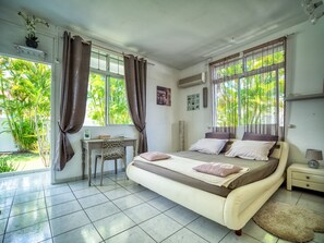 A bedroom with a bed, a desk, and a chair. There are windows with curtains, a picture on the wall, and a small table with a lamp. - Aline, villa with swimming pool and jacuzzi, close to all amenities (Le Gosier)