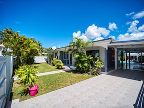 A modern house with a covered patio, a swimming pool, and lush greenery.