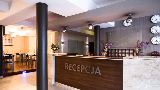 Un área de recepción con mostrador de madera, varios relojes y una zona de estar con mesas y sillas.