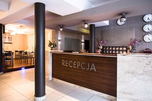 A reception area with a wooden counter, multiple clocks, and a seating area with tables and chairs. - Hotel & Spa Kameleon (Zory)