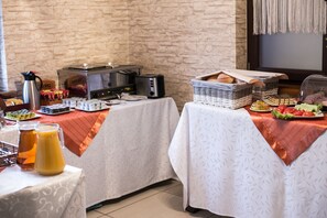 A breakfast buffet setup with various food items and beverages, including a coffee maker, toaster, and baskets of bread. - Hotel & Spa Kameleon (Zory)