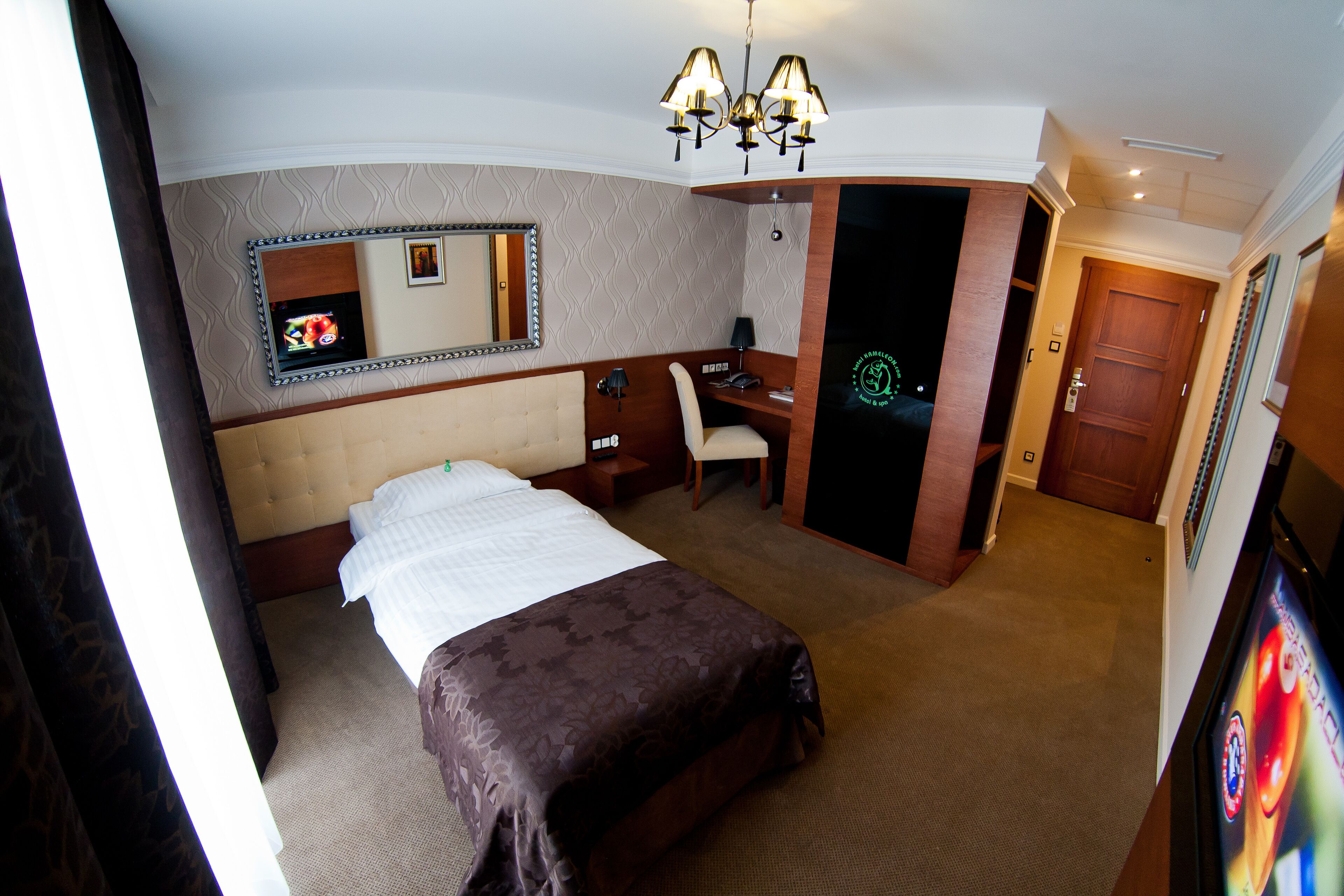 Una habitación de hotel con cama, escritorio, silla, espejo y puerta.