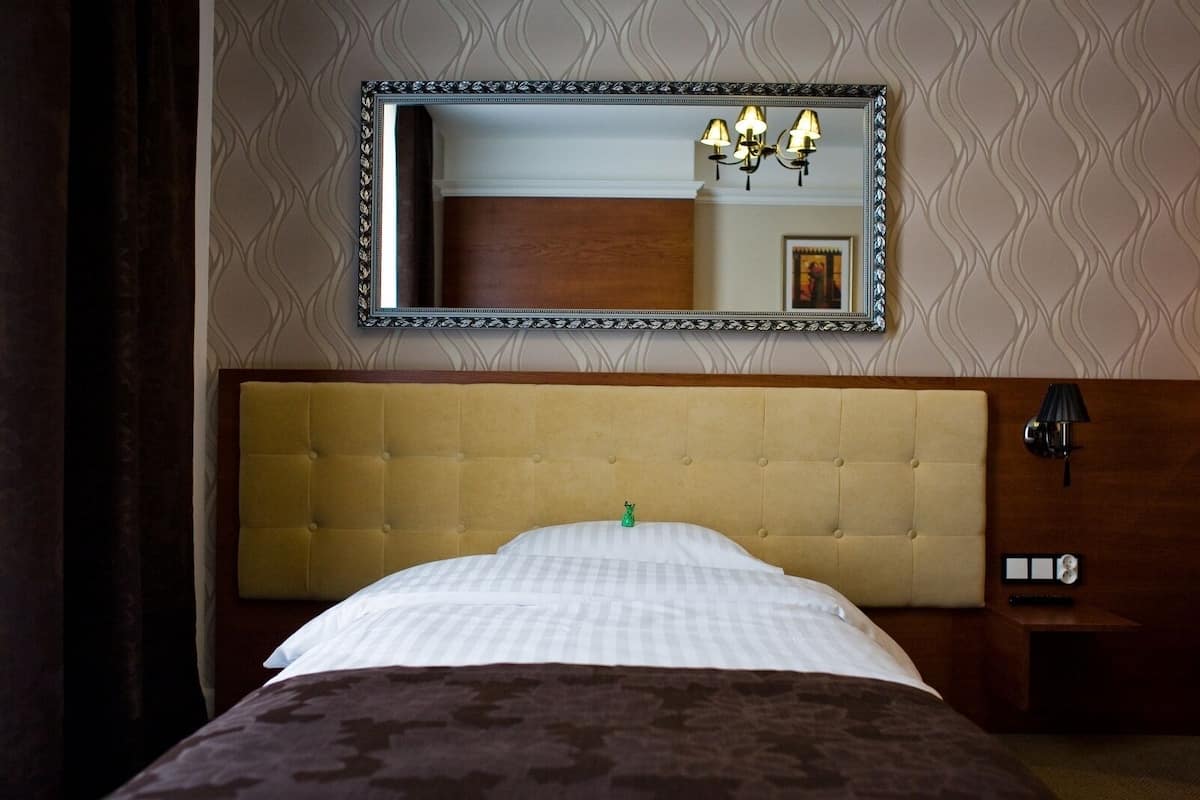 A hotel room with a large bed, a tufted headboard, a nightstand with a lamp, and a wall-mounted mirror.