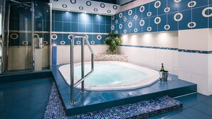 Un área de piscina interior moderna con ducha envuelta en vidrio, jacuzzi y pared de azulejos con diseños circulares.