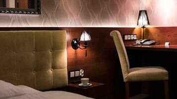 A hotel room with a tufted headboard, a bedside table with a lamp, a chair, and a small table with a cup of coffee.