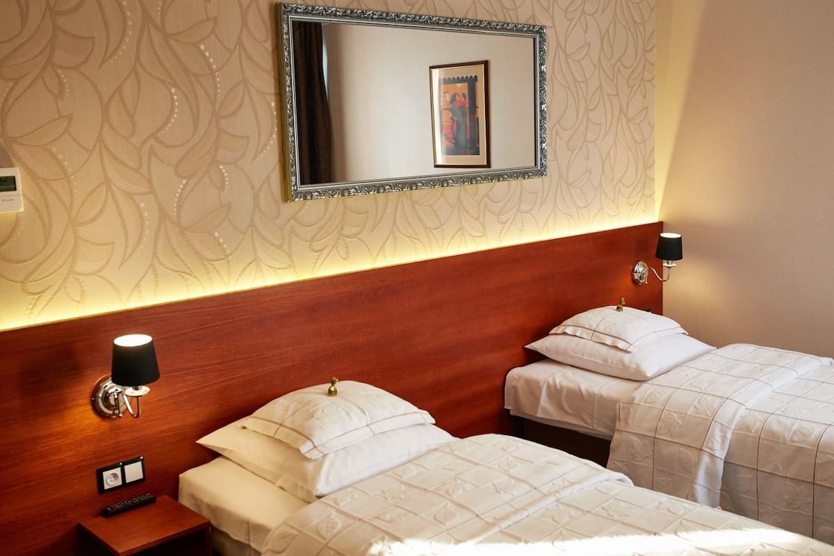 A hotel room with two beds, a wooden headboard, a wall-mounted mirror, and a bedside lamp.