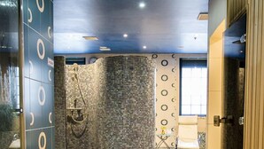 Un pasillo con diseño de suelo de mosaico, zona de ducha con patrón circular de azulejos y un área de descanso con una silla y una mesa.